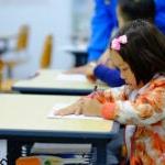 A young student sits at a desk with a pencil in her hand.